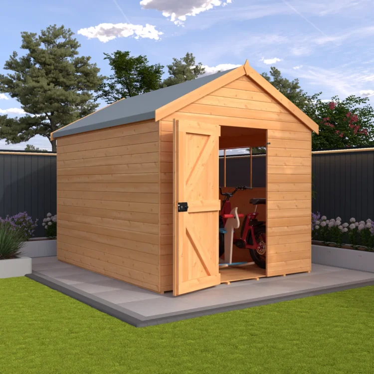 A wooden shed with a grey roof and open door on a concrete slab in a garden with green grass and flowers