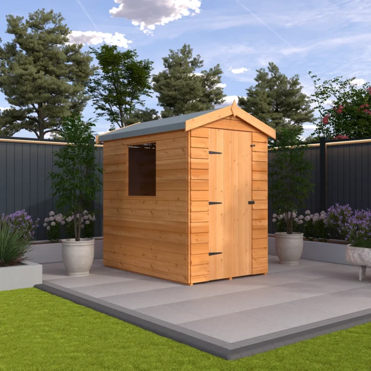 A small wooden shed with a grey roof and patio area in a backyard with plants and a fence on a sunny day