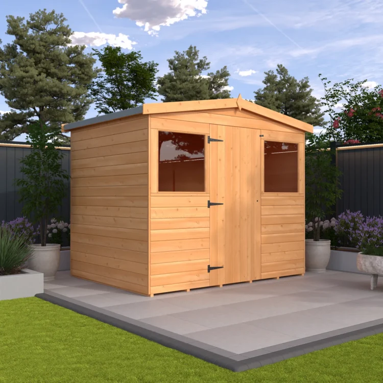 A small wooden shed with two windows and a door on a patio surrounded by plants and a fence under a blue sky