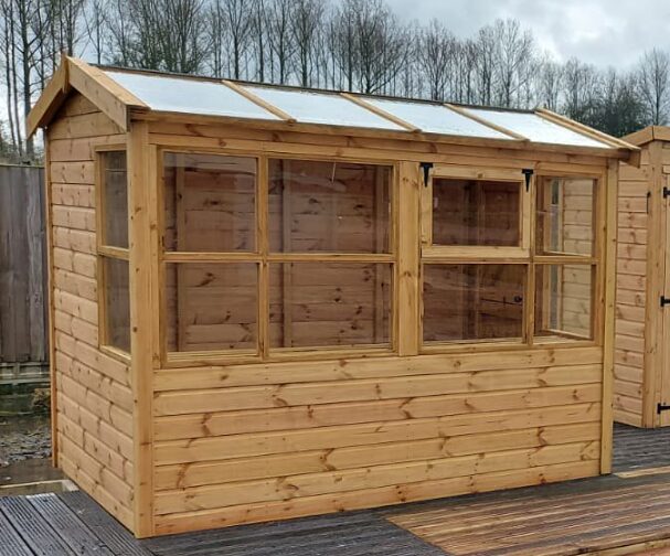 A wooden shed with glass panels on a deck, surrounded by trees under a cloudy sky